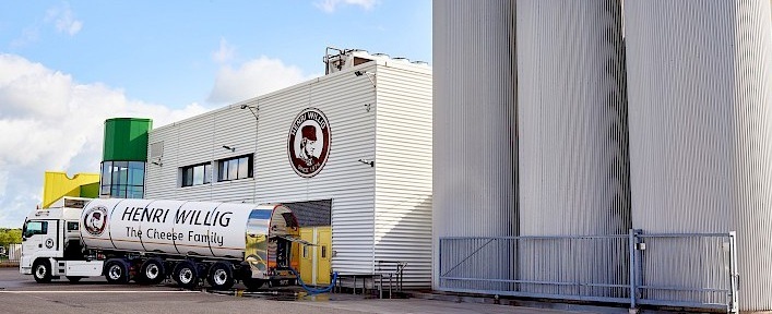 Fabrieksgebouw met silo's en een vrachtwagen met het logo van Henri Willig - kaasmakerij